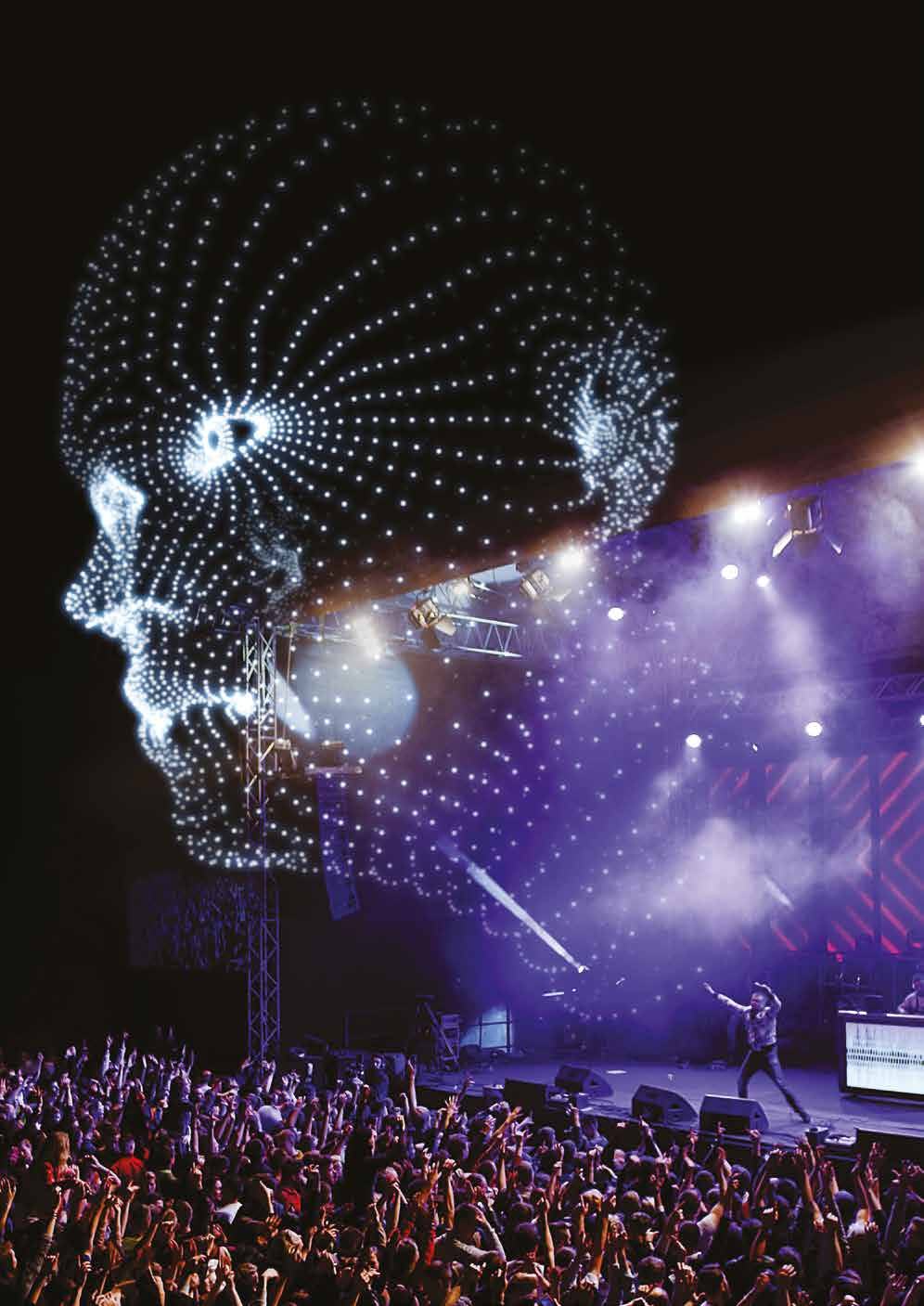 Crowd at a concert with a performer on stage, beneath a large glowing wireframe projection of a human head.