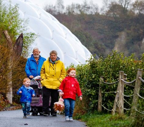 A family, including two adults and two young children, walks on a path outdoors with large geodesic domes in the background.