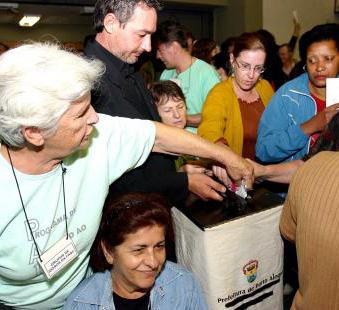 A woman casts her vote into a ballot box surrounded by other community members.