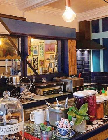 Interior view of a cafe counter with various food items, jars of ingredients, a coffee machine, and other kitchen equipment.