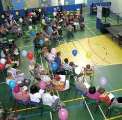 Aerial view of a large group of people seated on a basketball court for an event or assembly, with colorful balloons scattered around.