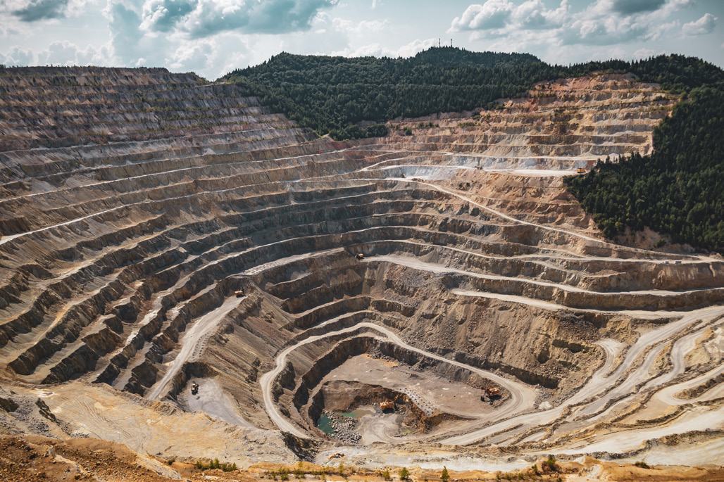 Aerial view of a large open-pit mine with multiple terraced levels and heavy machinery, showing the scale of resource extraction.