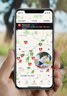 Hand holding a smartphone displaying the GoodSAM app map with emergency icons and an alert notification.
