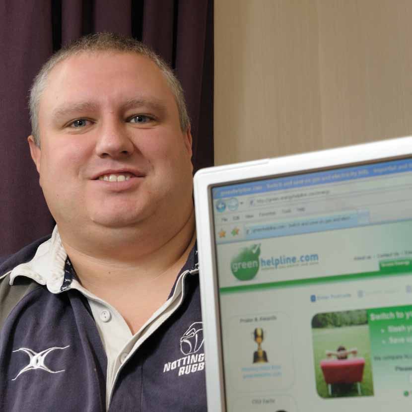A man smiling, with a laptop screen partially visible showing the "greenhelpline.com" website.