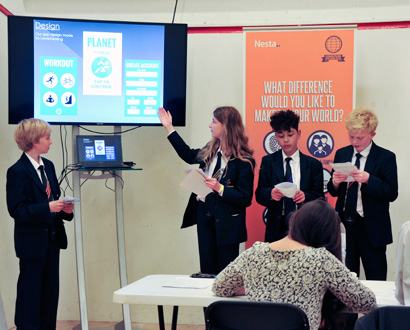 Students presenting a mobile app design on a large screen, showing user interface elements for a fitness application during a project presentation.