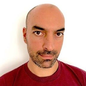 Headshot of a man with a beard, wearing a red t-shirt, looking forward.