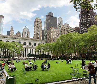 An urban park with a large green lawn filled with people relaxing and socializing, surrounded by tall buildings.