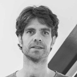 Black and white headshot of a man with curly hair and a beard, looking slightly to the right.