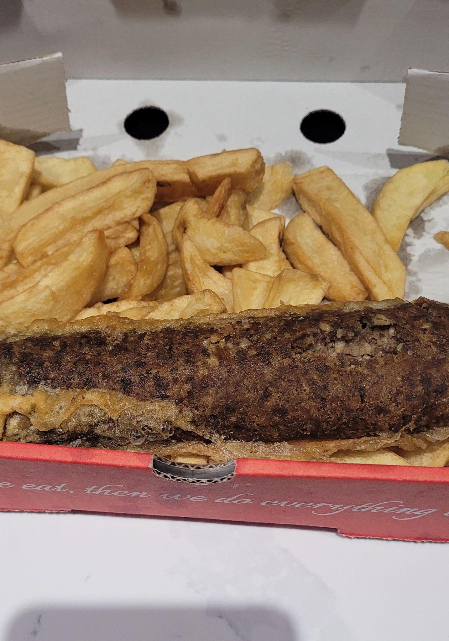 Deep-fried haggis and chips in a takeaway box.