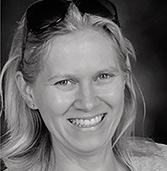 Black and white headshot of a smiling woman with blonde hair and sunglasses on her head.