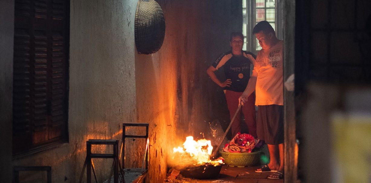 Two people in a dim room tending a small fire on the floor, one stirring items in a basket.