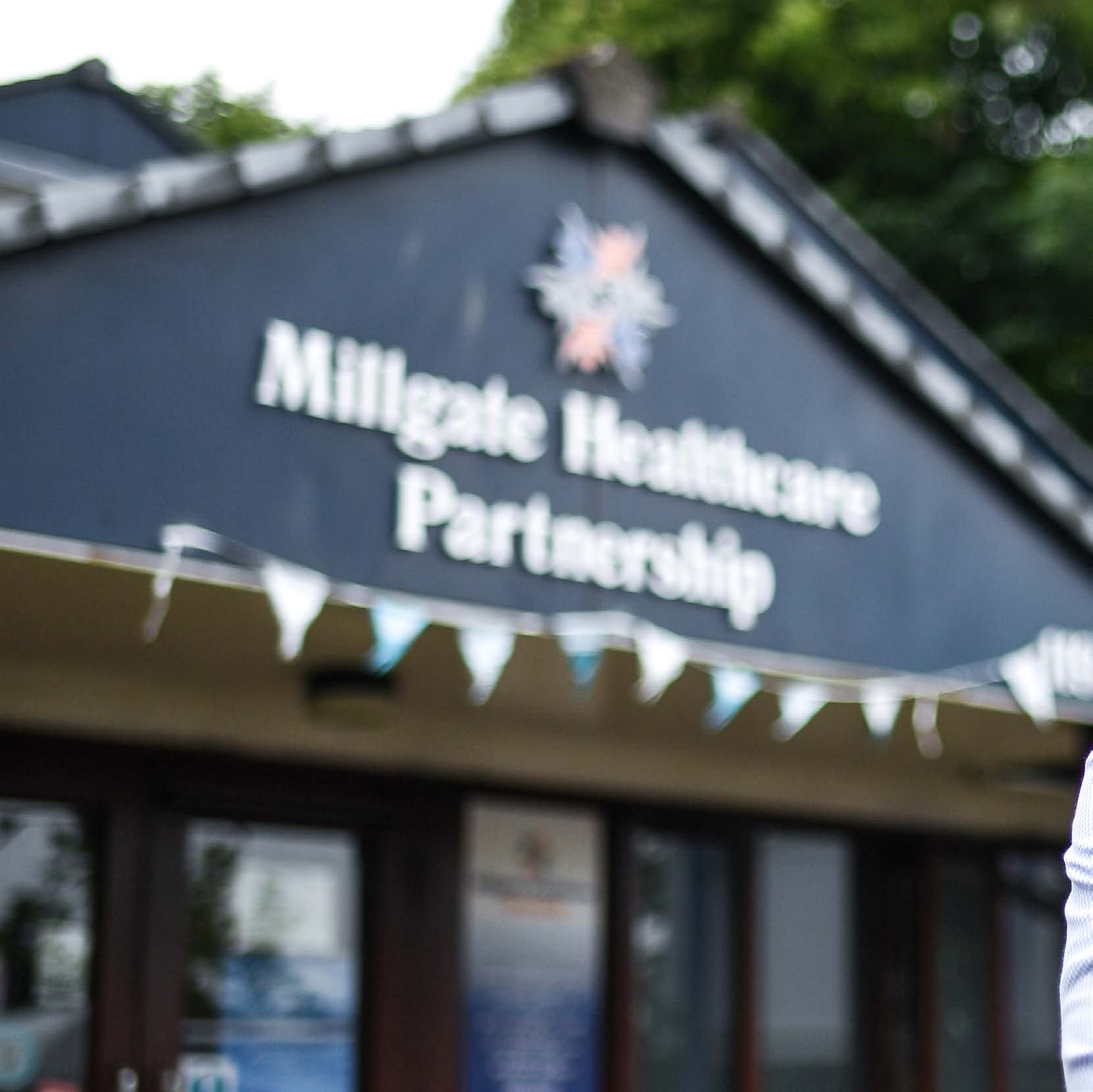 Exterior view of the Millgate Healthcare Partnership building with its sign and logo clearly visible.