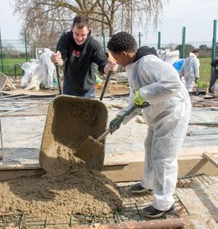 Two men pouring concrete from a wheelbarrow onto a rebar grid during an outdoor construction or volunteering project.
