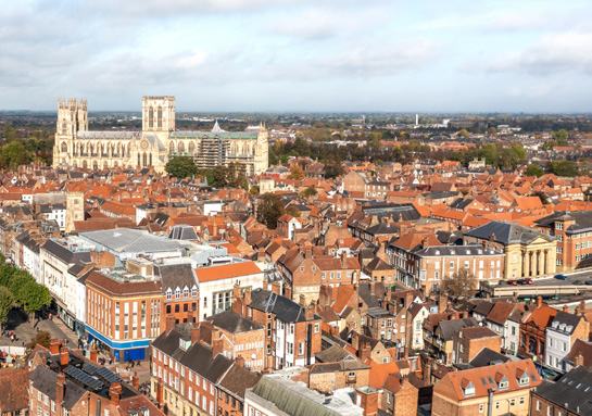 An aerial view of a historic city featuring numerous red-roofed buildings and a large, ornate cathedral with twin towers, likely York Minster.
