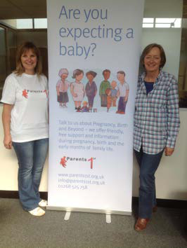 Two women standing next to a "Parents 1st" banner advertising support for expectant parents, providing contact information.