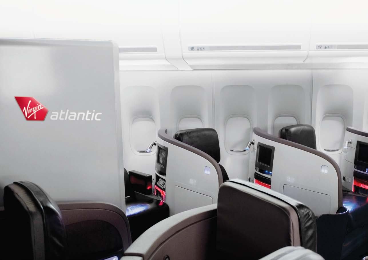 Interior view of a modern Virgin Atlantic aircraft cabin with rows of premium seats and entertainment screens.
