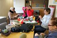 Women knitting around a table, engaged in a group activity.