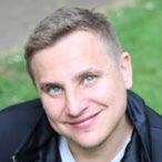 Headshot of a smiling man with short blonde hair and blue eyes, possibly a staff member or featured individual.