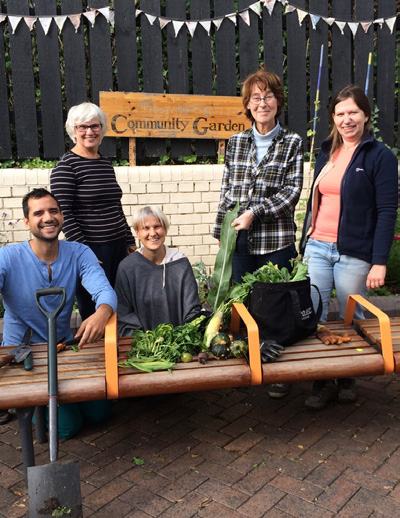 Five people, smiling, with a fresh harvest of vegetables from a community garden.