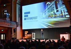 A speaker on stage at the Futurefest event, presenting in front of a large screen displaying the event logo and a cityscape.