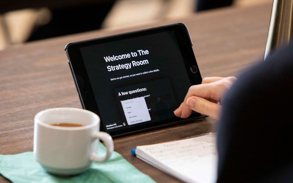 Hands interacting with a tablet displaying a "Welcome to The Strategy Room" screen, showing a gender selection question.