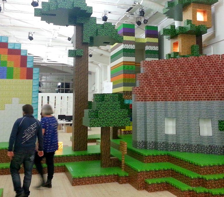 Interior view of an exhibition featuring large-scale, block-like structures inspired by the video game Minecraft, with visitors.