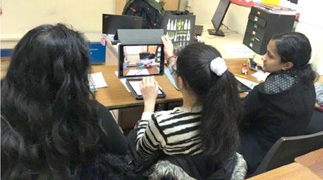 Three people, including a child, sitting around a table with tablets, engaged in an activity; the child is actively interacting with a tablet.