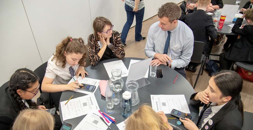 Students and an adult engage in a collaborative learning session around a round table, working with papers and calculators.