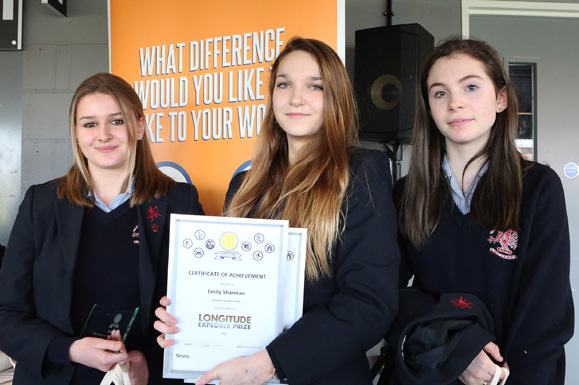 Three female students, one holding a "Certificate of Achievement" for the Longitude Explorer Prize, smiling for the camera.