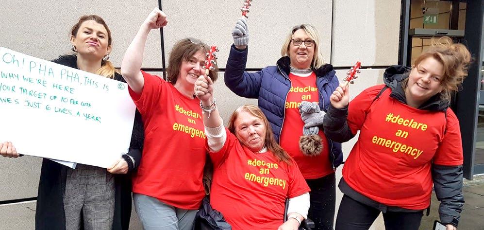 Five women, mostly wearing "declare an emergency" t-shirts, pose outdoors; one holds a sign about traffic fatalities.
