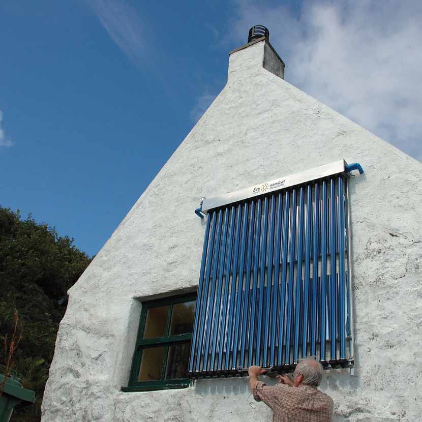 A man adjusting a vertical solar thermal collector installed on the side of a white house.