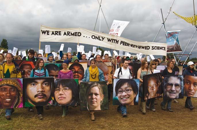 Protestors marching with a banner reading "WE ARE ARMED... ONLY WITH PEER-REVIEWED SCIENCE" and holding signs with large photographic portraits.