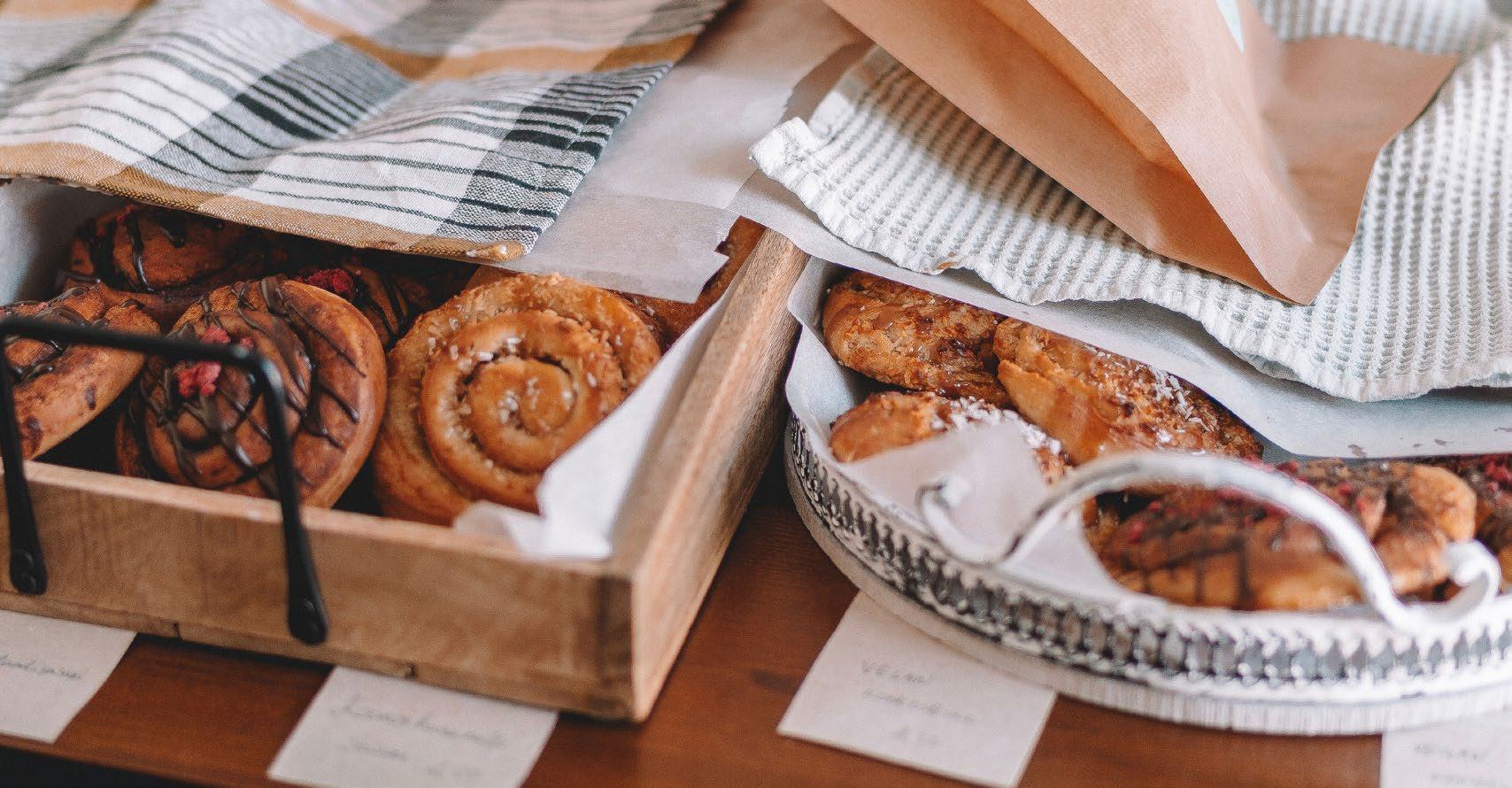 Assortment of baked goods, including cinnamon rolls and pastries, displayed in wooden boxes and on a silver tray.