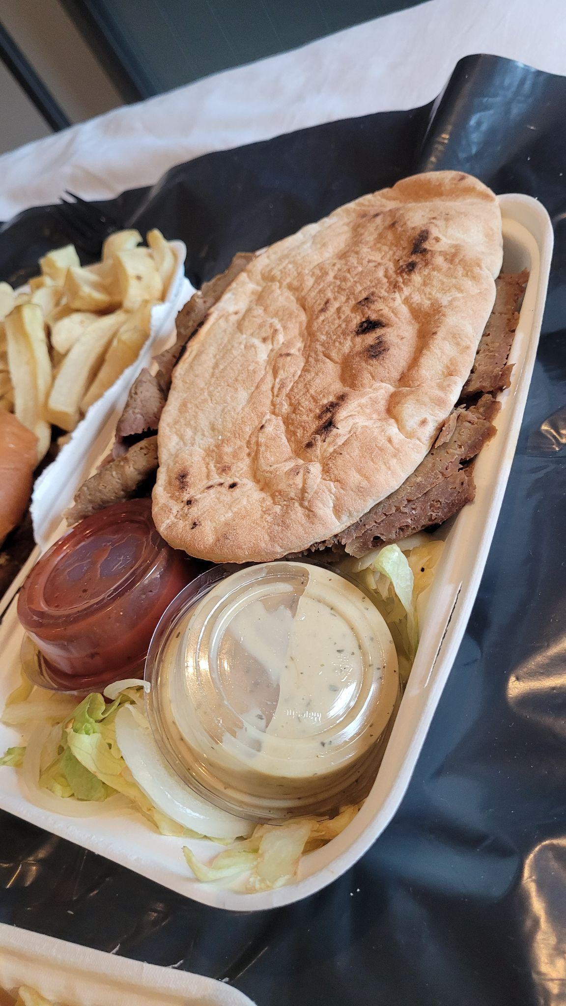 Kebab with flatbread, meat, salad, and sauces in a takeaway container, with chips.
