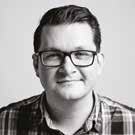 Headshot of a man with glasses and a plaid shirt, smiling slightly.