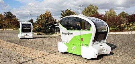 Two white and green UKAutodrive autonomous shuttle buses on a paved area.