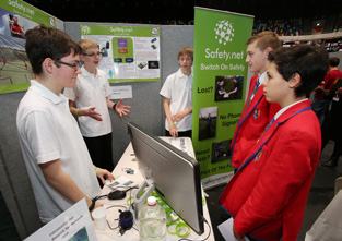 Students interacting at an exhibit booth, looking at a computer monitor and display boards for a project called "Safety.net Switch On Safety."