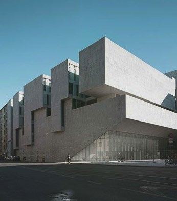 Exterior view of a modern building with stark concrete blocks and glass facades, under a clear blue sky.