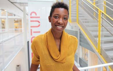 Smiling woman with short dark hair, standing in a modern building with stairs and a "STARTUP" sign.