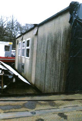 A weathered, dirty portable cabin or modular building with windows, situated next to discarded materials outdoors.