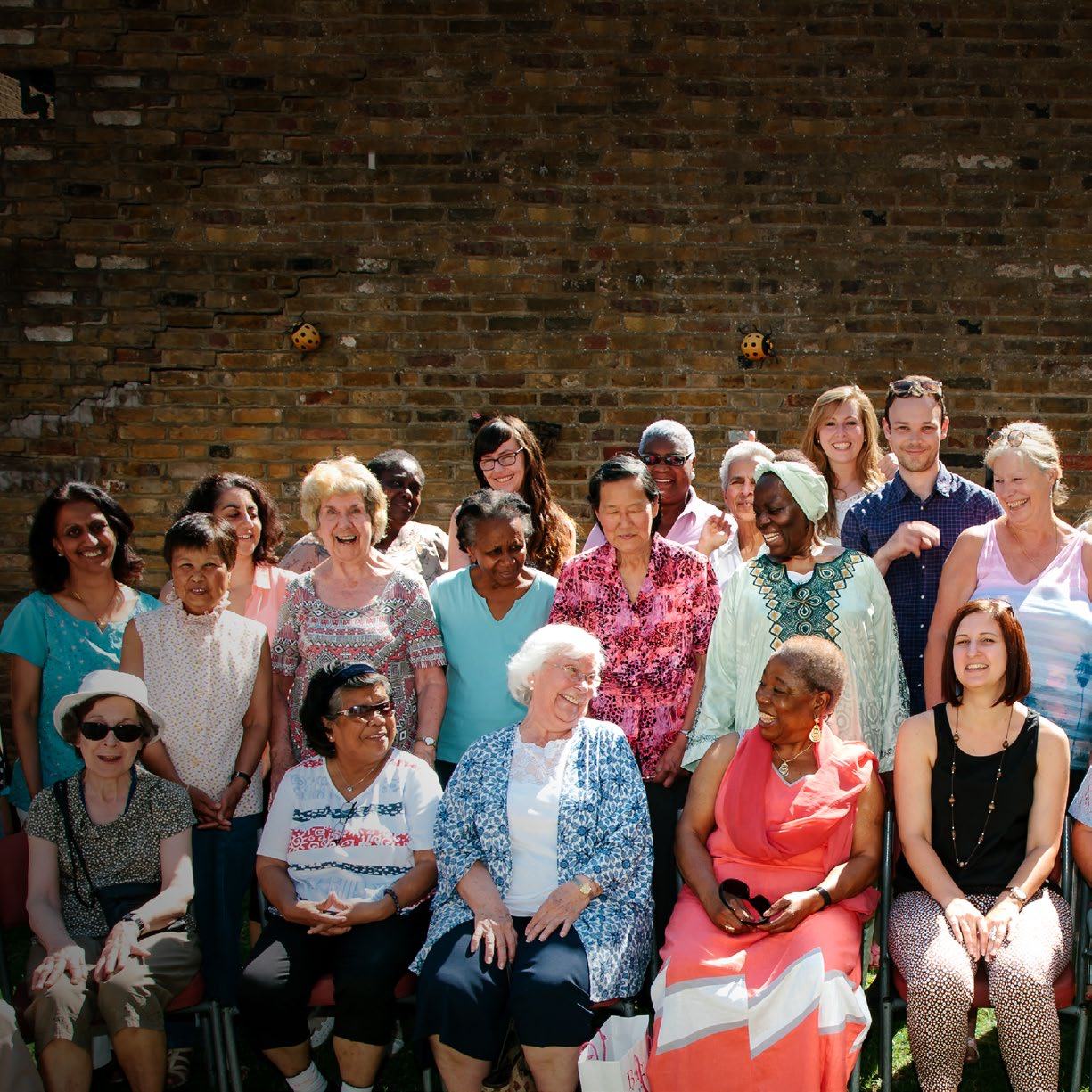 Group photo of diverse community members, mostly women of varying ages, smiling outdoors.