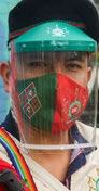 Man in a green face shield, green and red patterned face mask, and dark beret.