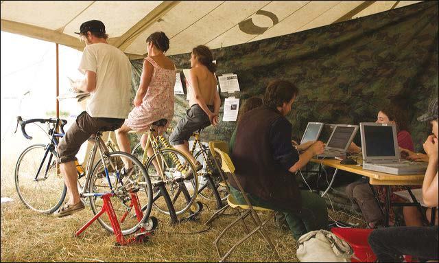 People use stationary bikes to generate power, while others work on laptops at a table inside a tent.