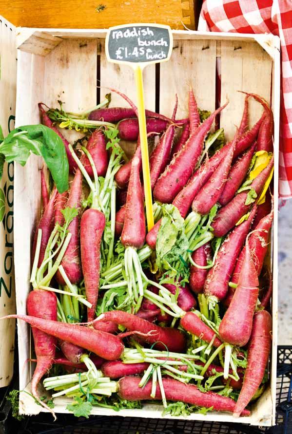 A wooden crate filled with fresh red radishes, with a price tag showing "raddish bunch £1.45 /bunch"