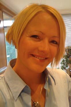 Close-up portrait of a smiling woman with short blonde hair and a light blue collared shirt.
