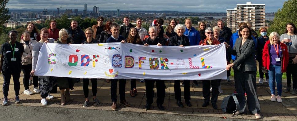 Group of people holding a "GOOD FOR ALL" banner with a city skyline in the background.
