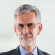 Headshot of a man with gray hair, glasses, and a suit jacket and collared shirt.