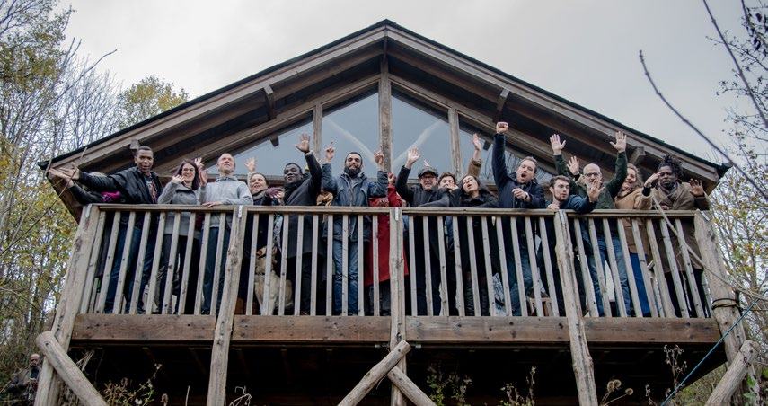 A diverse group of people on a rustic wooden cabin balcony, waving and celebrating.