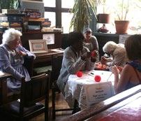 Older adults gathered in a room, some engaged in crafting at tables, suggesting a community social event.