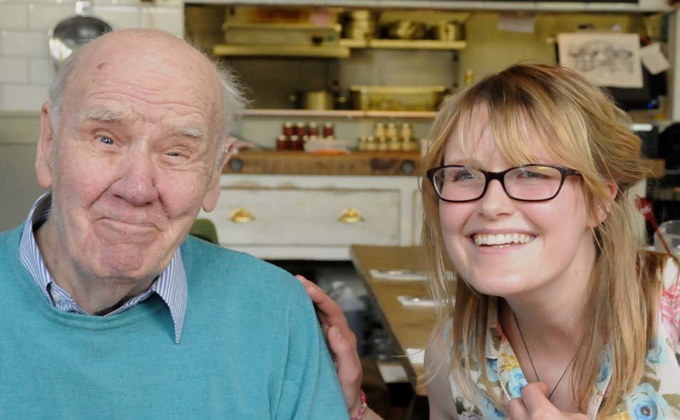A smiling older man in a blue sweater next to a smiling younger woman in glasses, illustrating intergenerational connection.